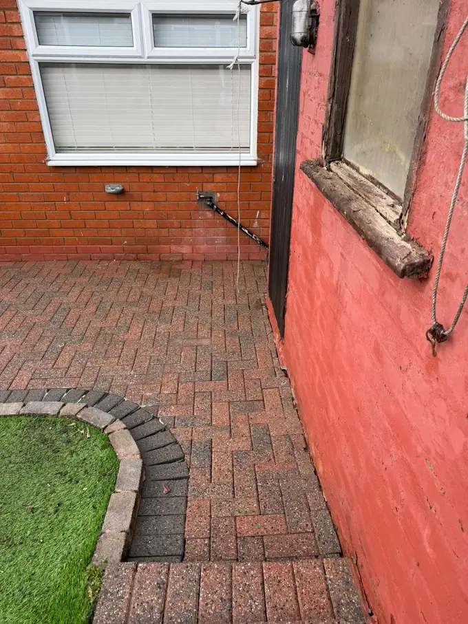 Red block paving path cleaned alongside a rendered house